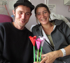 Young couple in a hospital room smile and hold their origami flowers