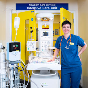 Young woman in scrubs smiles beside medical equipment