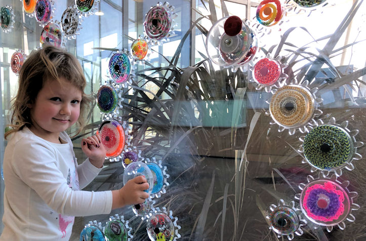 Child by large glass window playing with colourful cogs embedded in the glass
