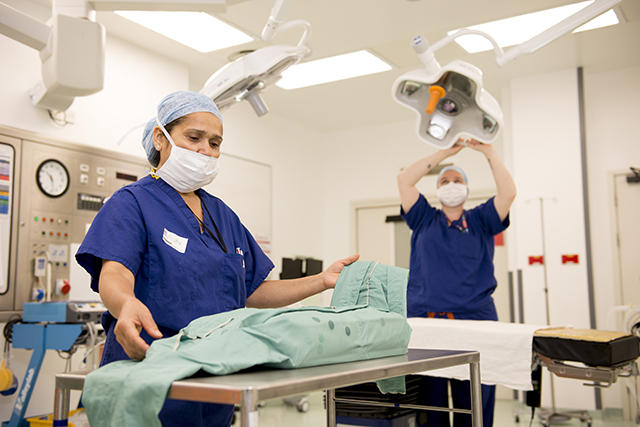 Two people in scrubs and face masks prepare a theatre for surgery
