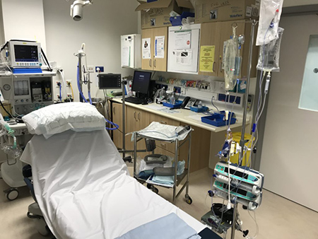 Clinic room with bed, monitors, medical equipment, desk and cupboards