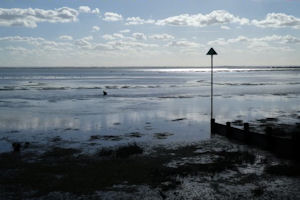 Clouds reflected in calm sea, beyond beach with single signpost