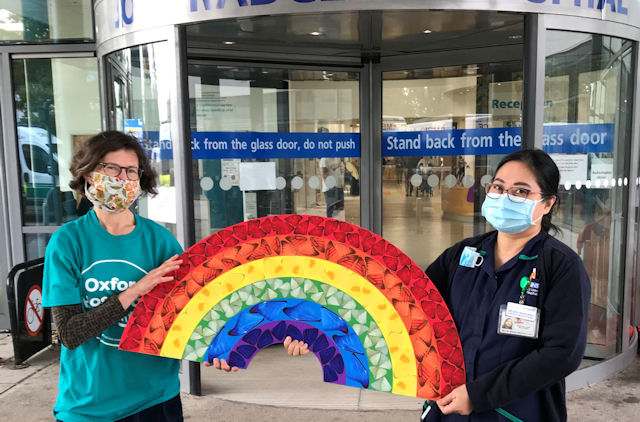 Two women in face masks hold up large rainbow picture