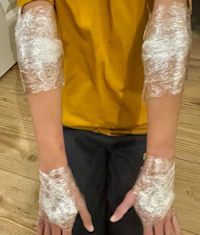 Kneeling child's elbows and hands are thoroughly wrapped in layers of cling film