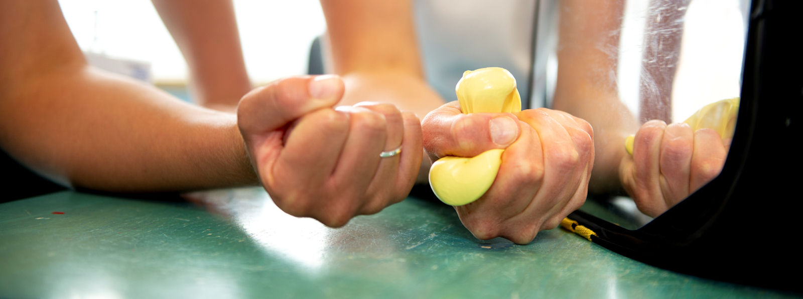 Hands squeeze a ball on a table in front of a mirror