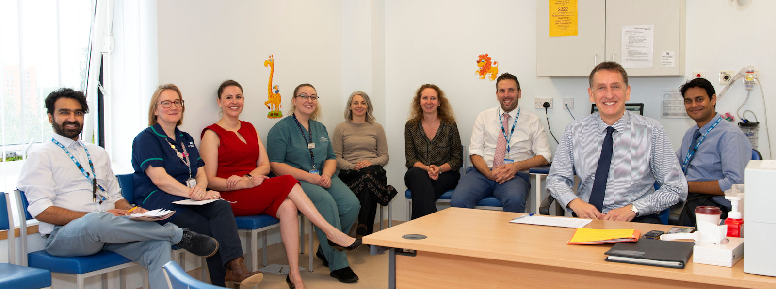 Nine professionals with lanyards seated smiling in a clinic room