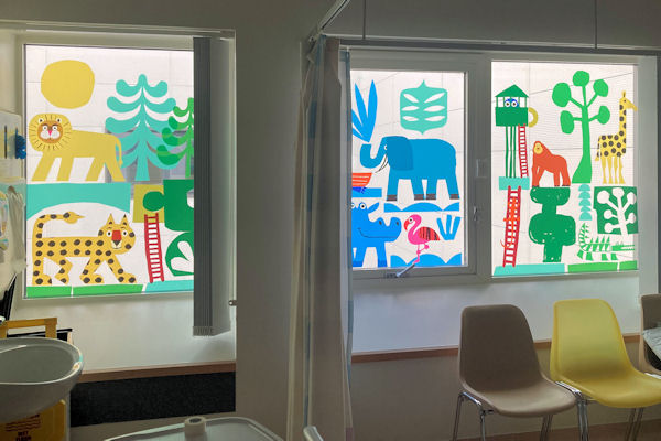 Three translucent window panels in a dim waiting area featuring naive images of  jungle and savannah animals.