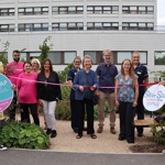 Eleven people in the new garden. One person is about to cut the ribbon. Two people hold banners for 'Silver Star Maternity Fund' and 'SSNAP'