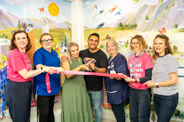 Group of seven smiling people. A couple are cutting a pink ribbon and two people are wearing pink 'Oxford Hospitals Charity' t-shirts.