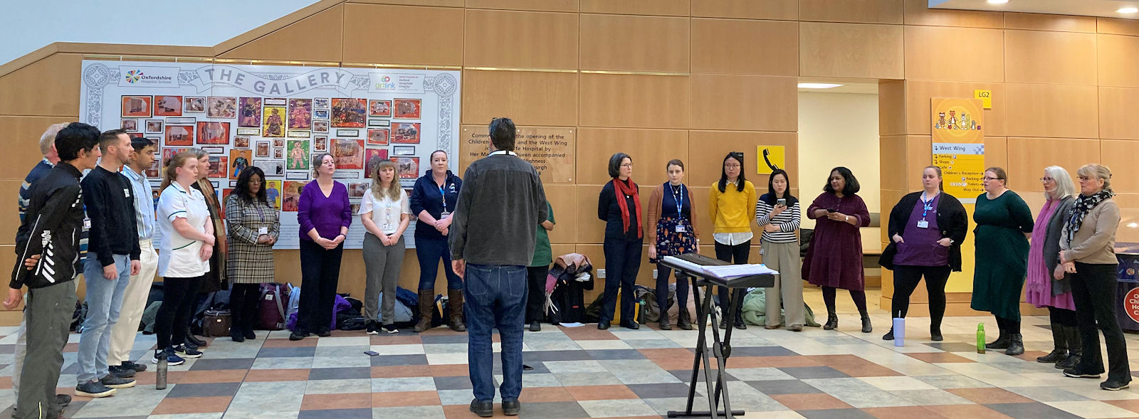 20 people informally dressed stand in a row in the West Wing atrium.