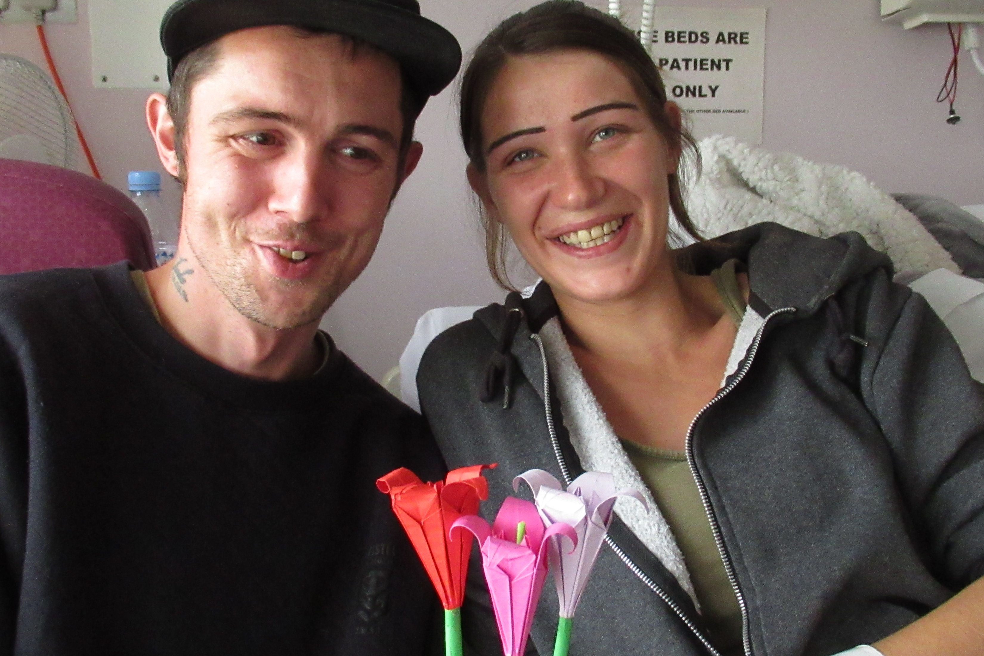 Young smiling couple in hospital room with three paper flowers.