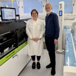 Man and woman stand in laboratory in front of analyser machine
