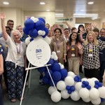 Group of 21 maternity staff gathered around a “50 years of service” sign and blue-and-white balloons, raising their hands in celebration.