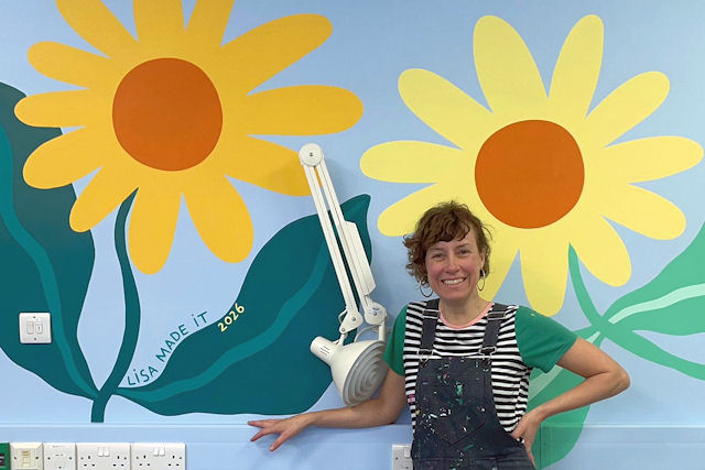 Two naive sunflowers painted on a wall with a smiling female artist in front of them