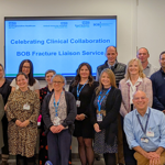 Group of NHS staff standing together in front of a presentation slide celebrating the BOB Fracture Liaison Service
