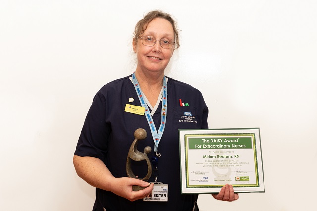 Miriam Redfern holding the DAISY award certificate and  a hand-carved sculpture - 'A Healer's Touch'.