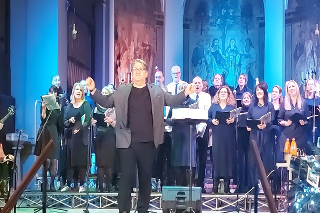 A conductor leading a large choir performing on stage inside a church