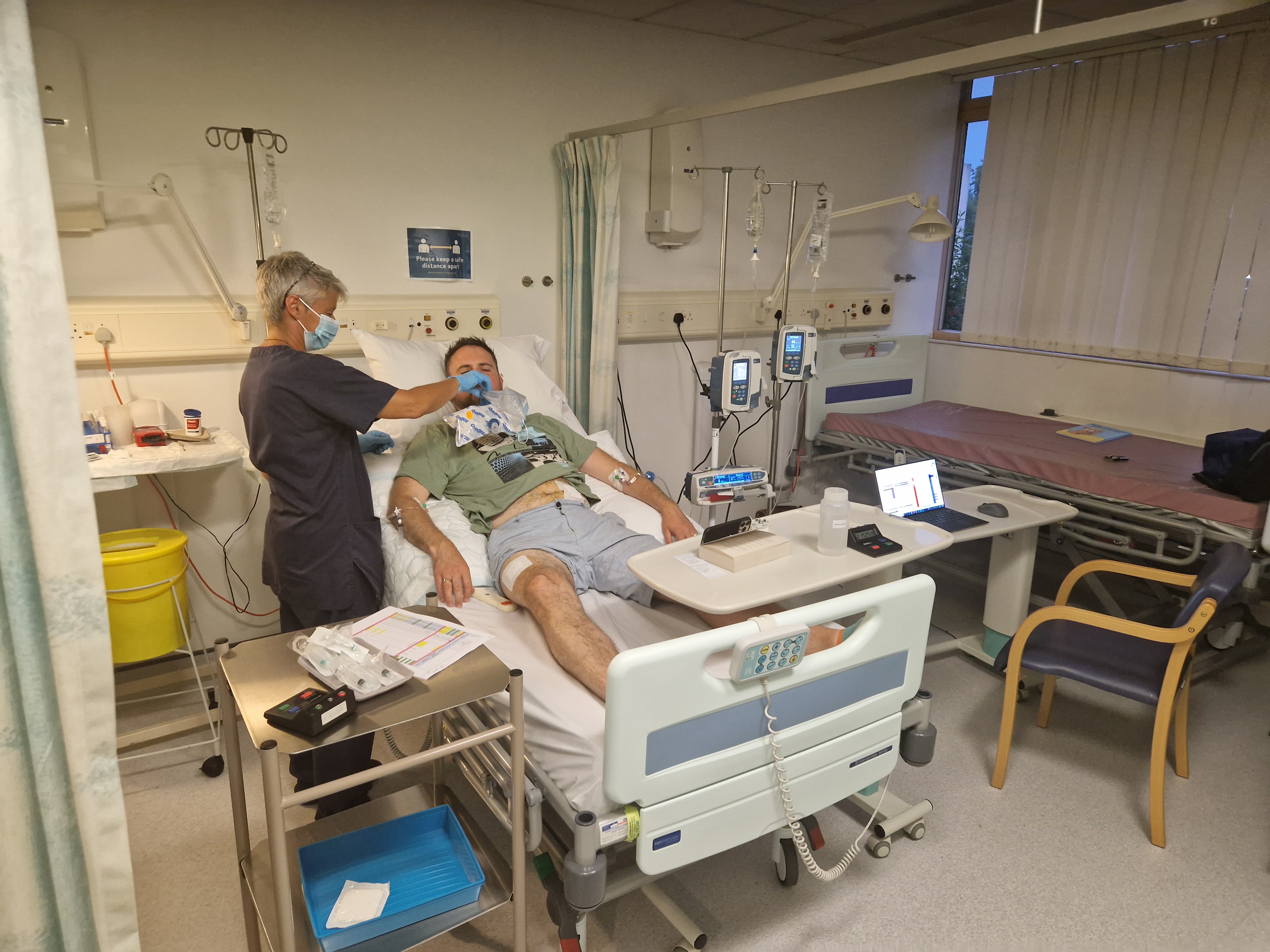 Female research nurse attends to male study participant undergoing tests in hospital bed 