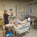 Female research nurse attends to male study participant undergoing tests in hospital bed 