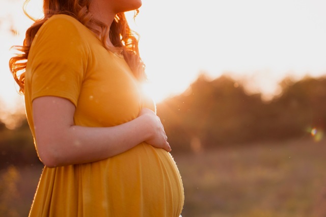 Woman in a yellow dress holding a baby bump outdoors at sunset