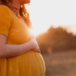 Woman in a yellow dress holding a baby bump outdoors at sunset