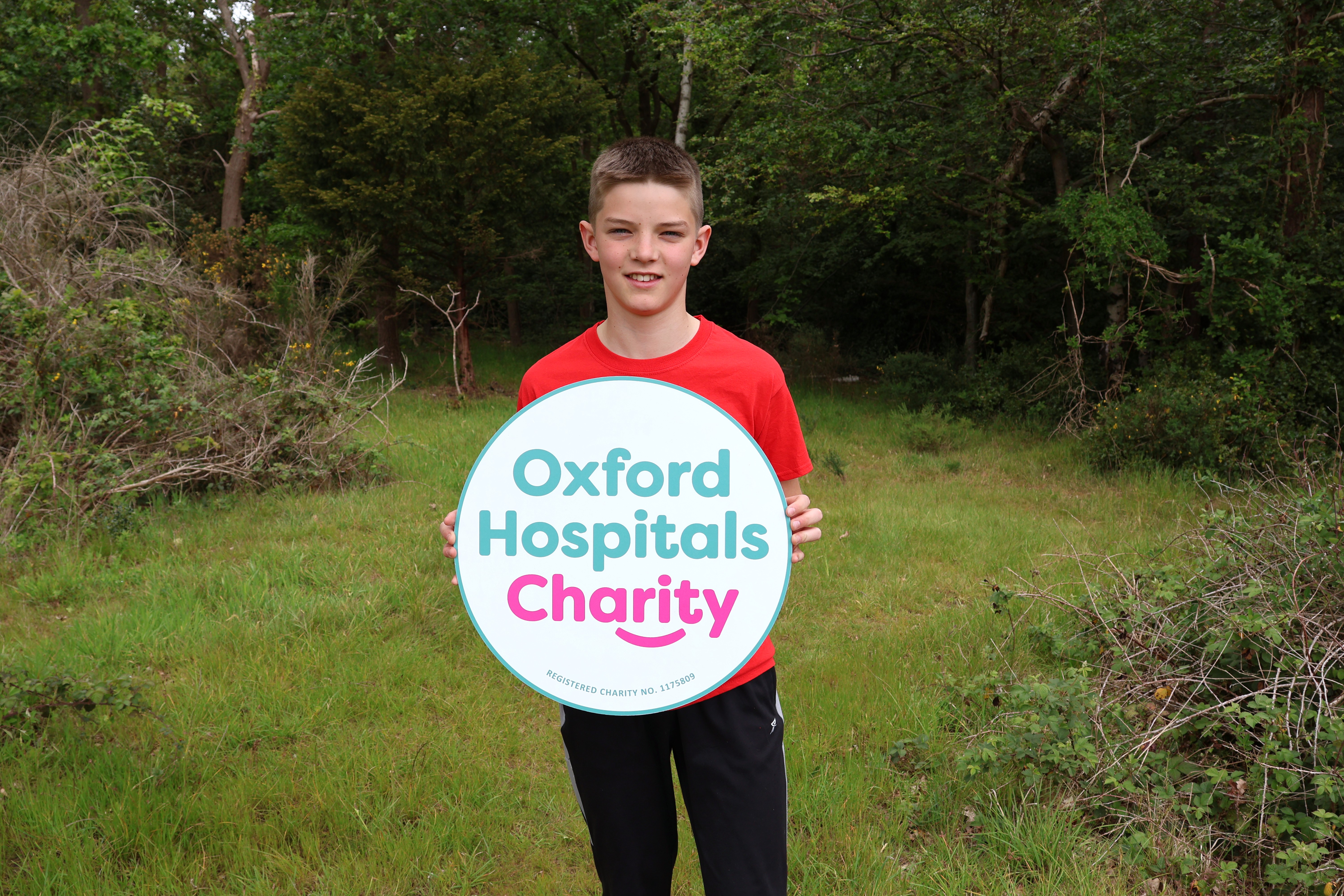 A child in a red T-shirt holds a large circular 'Oxford Hospitals Charity' banner