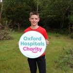 A child in a red T-shirt holds a large circular 'Oxford Hospitals Charity' banner