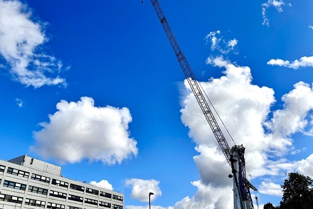 Construction crane next to a hospital building under a bright blue sky with scattered clouds.