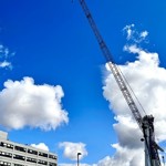 Construction crane next to a hospital building under a bright blue sky with scattered clouds.