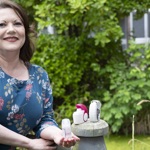 Woman holding an inhaler beside other inhalers, with green garden foliage in the background.