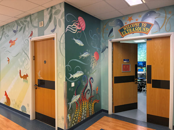 Two doors on a bend in a hospital corridor with bright sea creatures painted on the walls.