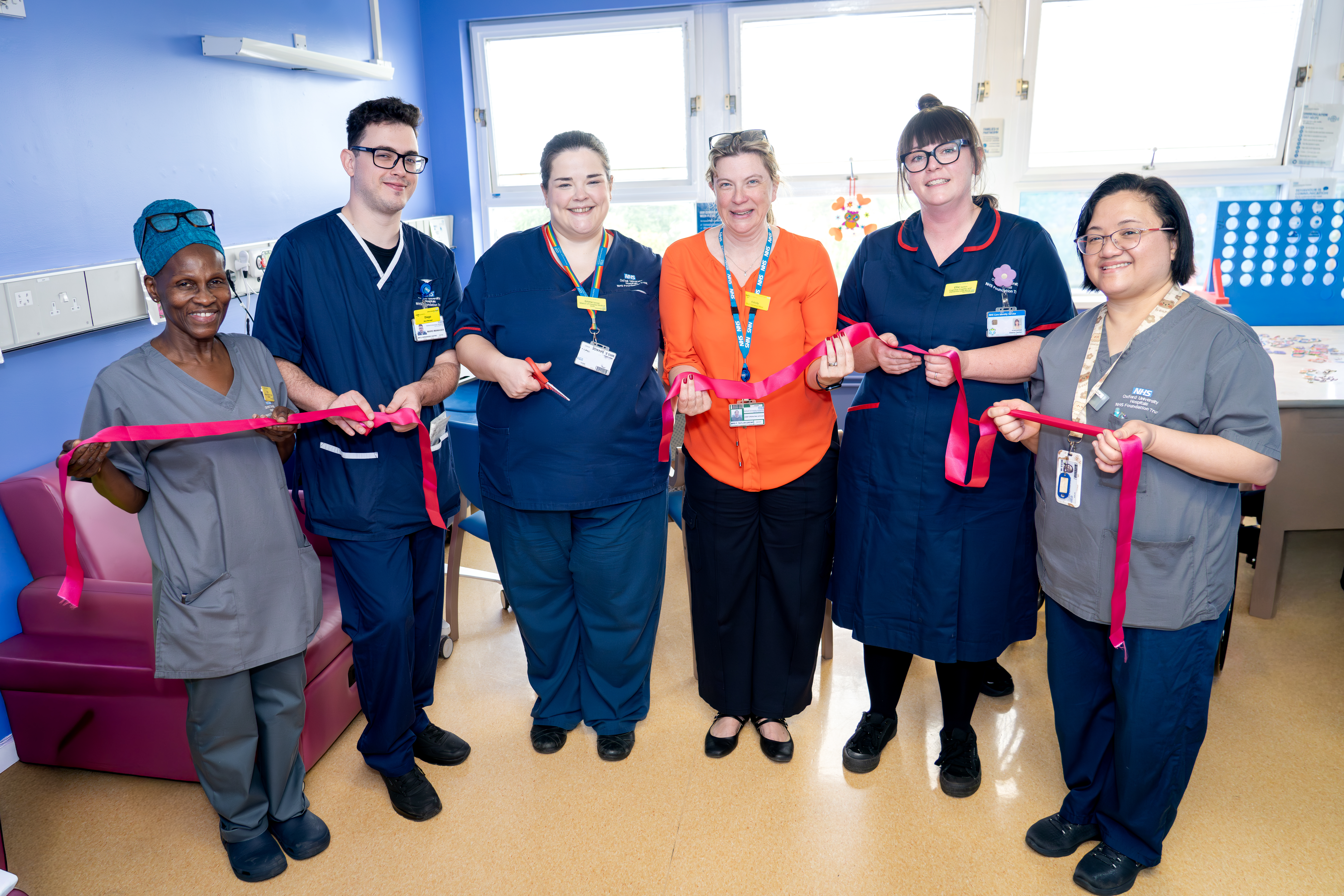 Healthcare staff hold a ribbon during a ribbon-cutting event in a hospital room.