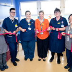Healthcare staff hold a ribbon during a ribbon-cutting event in a hospital room.
