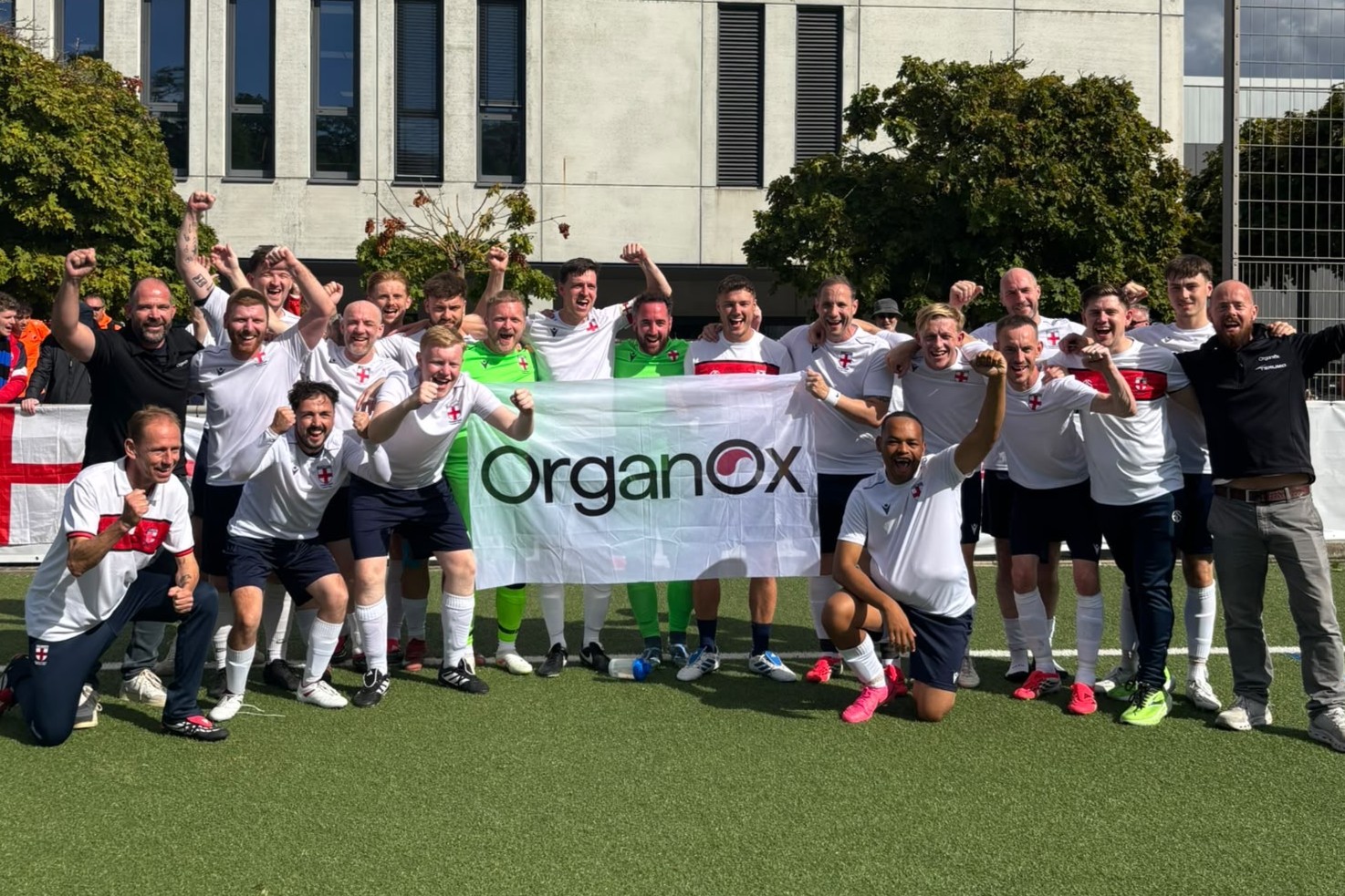 Group of football players and staff on a football pitch, celebrating. A large OrganOx banner is held up