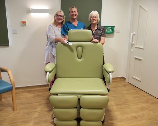 Three people behind a specialist green medical chair in a room with wooden flooring.