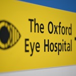 Black text on a yellow sign that reads: "The Oxford Eye Hospital". There is an image of an eye to the left and an arrow pointing right on the right