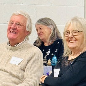 Older man and two older women with name stickers on their jumpers, smiling broadly.