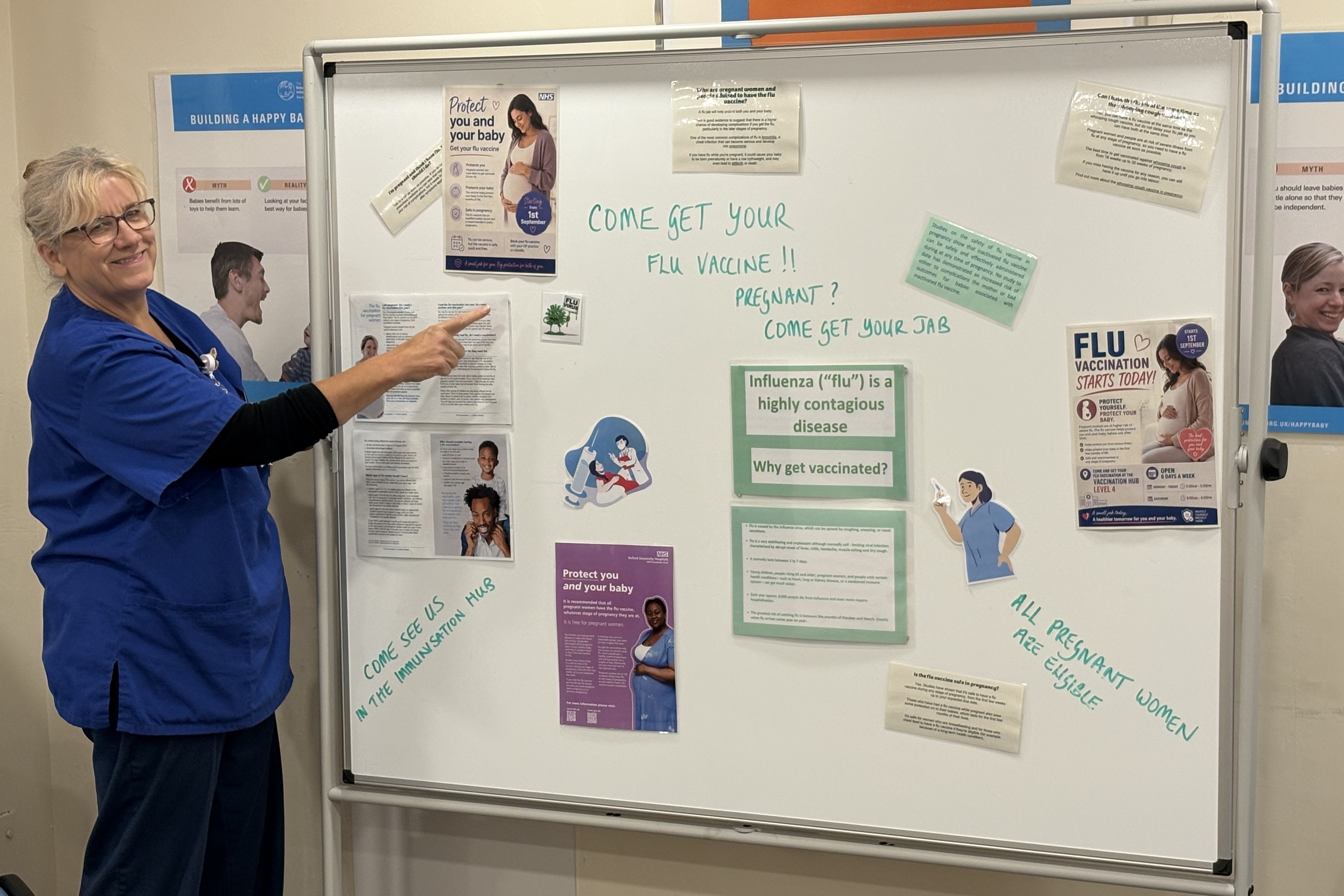 Staff member beside a flu vaccination information board, pointing to posters encouraging pregnant women to get their flu vaccine.