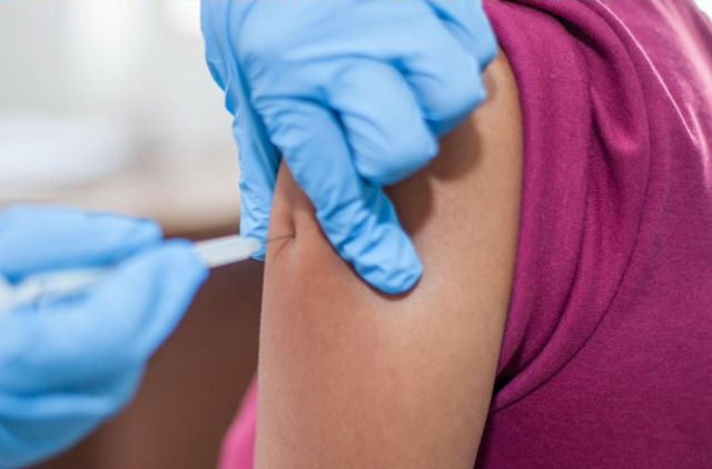 Medical gloved hands inject with syringe into female upper arm