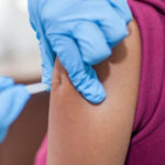 Medical gloved hands inject with syringe into female upper arm