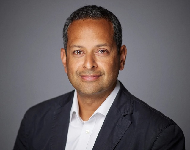 Headshot of Alpesh Kothari wearing a dark blazer and white shirt against a plain grey background, facing the camera.
