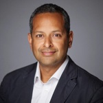 Headshot of Alpesh Kothari wearing a dark blazer and white shirt against a plain grey background, facing the camera.