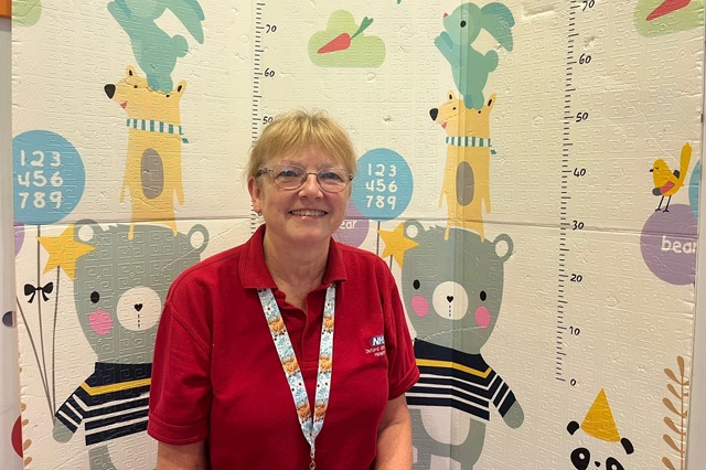 Sheila wearing her red 'play' uniform and in front of children's hospital play resources