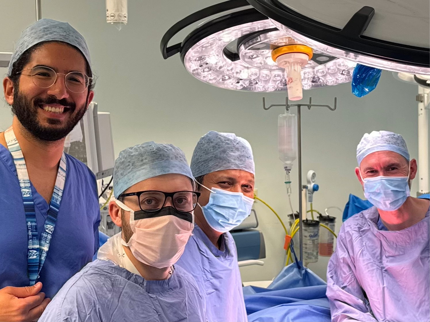 Four men wearing scrubs, three of them in surgical masks, in an operating theatre.