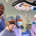 Four men wearing scrubs, three of them in surgical masks, in an operating theatre.