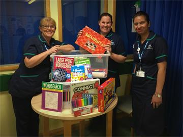 Three uniformed nurses open a plastic crate full of board games and puzzle books
