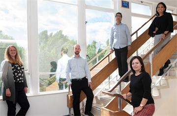 Five people standing well apart from each other on a modern staircase
