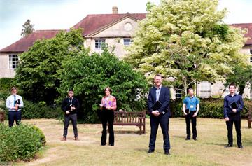 Six people spaced apart in a garden, old Manor House behind