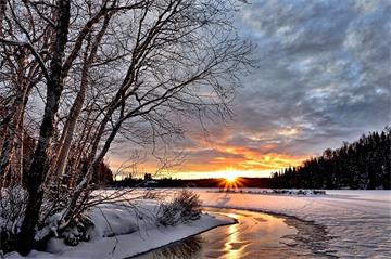 Snowy winter landscape of sun setting over stream with trees