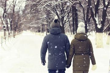 Two people in winter clothes hold hands and walk away down a snowy lane